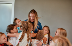 Female dance instructor is in the middle of a large group hug from her young dance students.